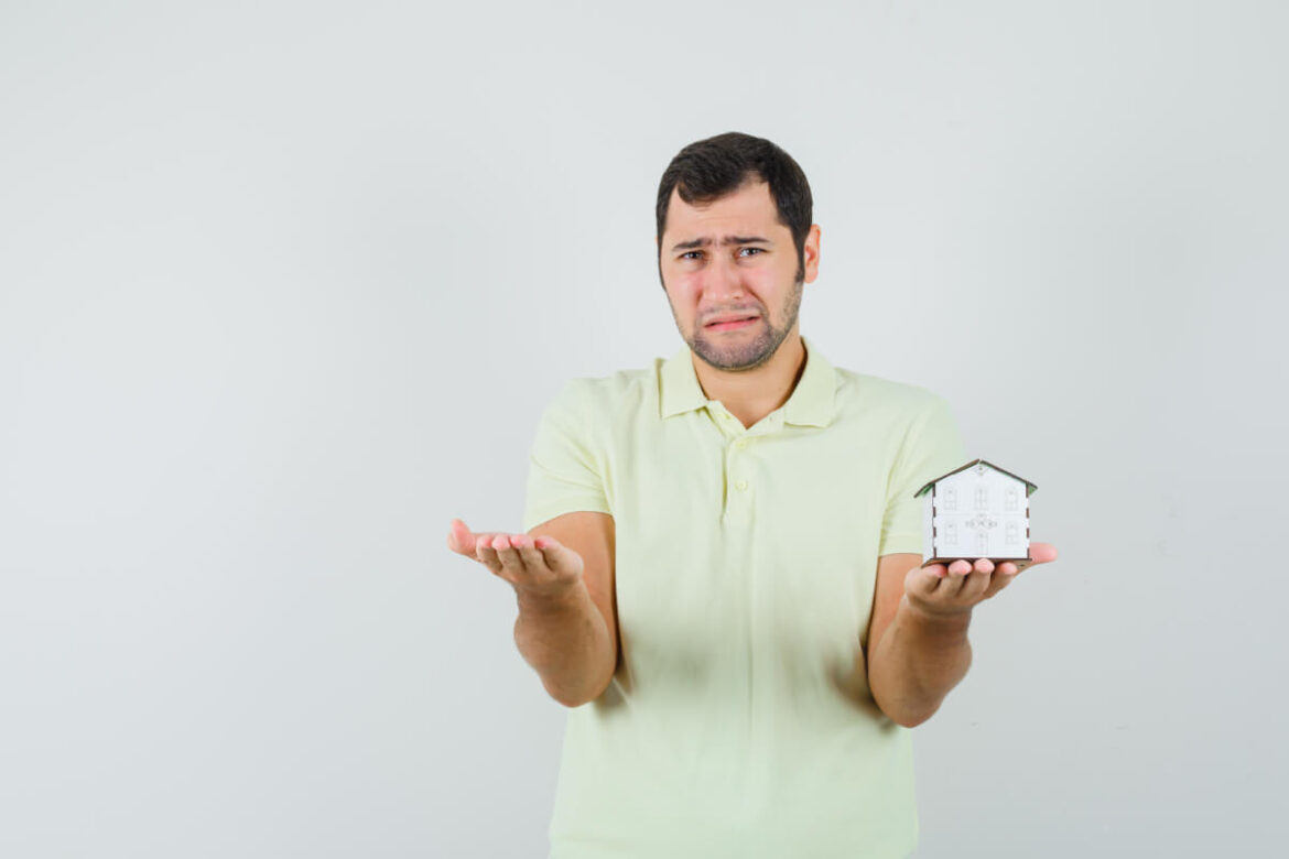 young-man-holding-house-model-spreading-palm-t-shirt-looking-disappointed (1) (1) Reasons Your House Is Not Selling